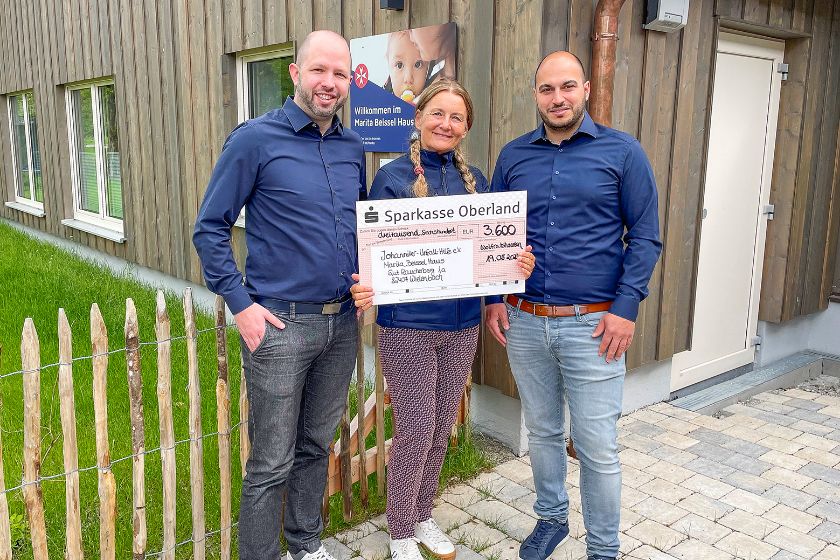 Eine Frau hält einen großen Spendencheck, rechts und links von ihr stehen zwei Männer.