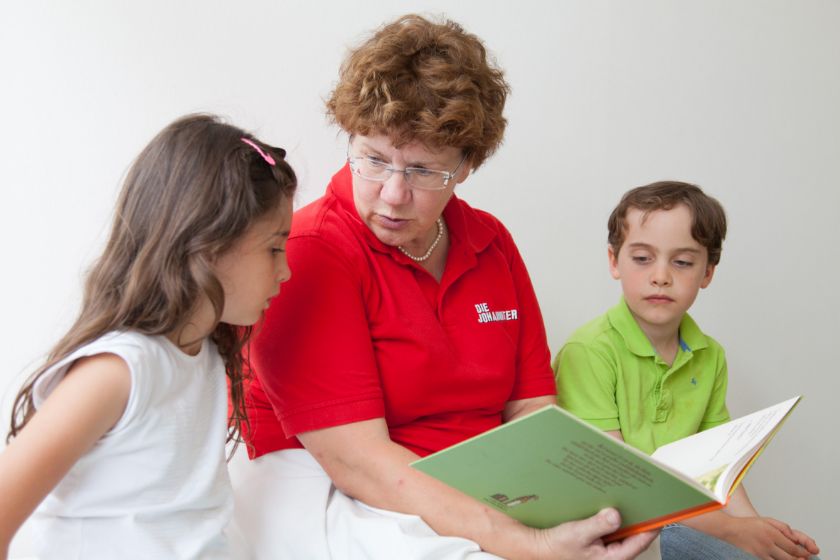 Eine Johannitern liest zwei Kindern aus einem Buch vor.