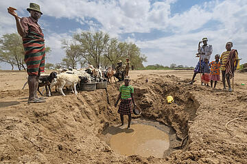 Menschen stehen um ein ausgetrocknetes Wasserloch herum.