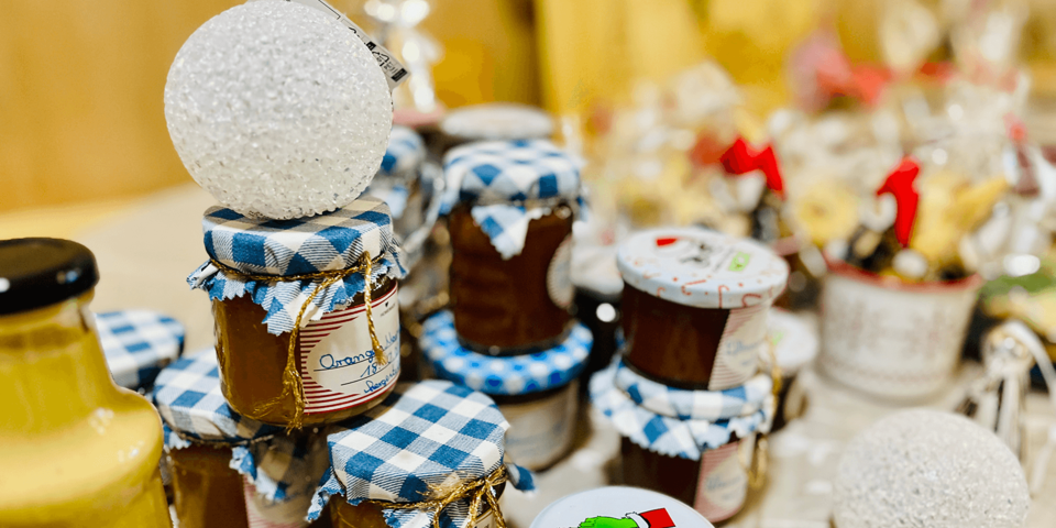 Verschiedene Marmeladengläser mit blau-weiß kariertem Stoffdeckel und handgeschriebenen Etiketten stehen auf einem Tisch, dekoriert mit winterlichen und weihnachtlichen Elementen.