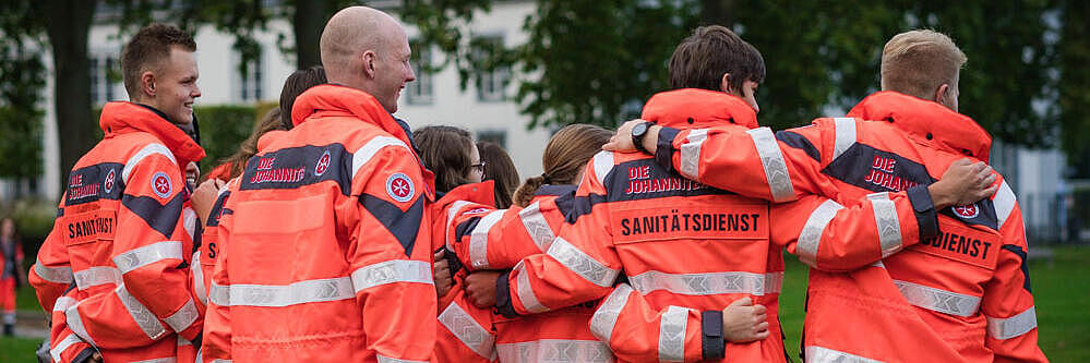 Gruppe Rettungssanitäter von hinten. Das Bild vermittelt ihre Motivation und den Zusammenhalt.