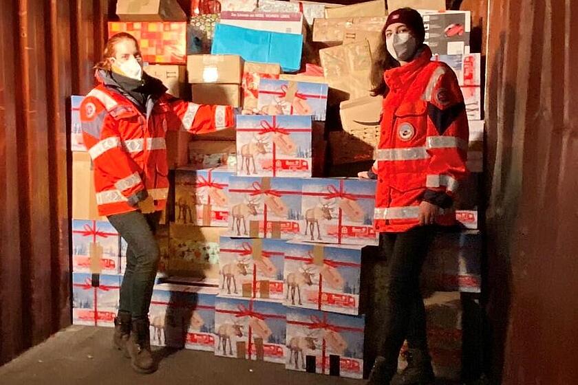 Zwei Johanniter-Helfer in roten Einsatzjacken stehen im Laderaum eines LKW und halten Kisten mit Hilfsgütern der Weihnachtstrucker Aktion.