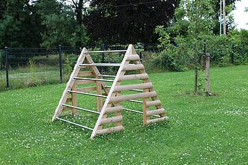 Klettergerüst in Dreieck-Form umgeben von einer schönen Grünfläche. 
