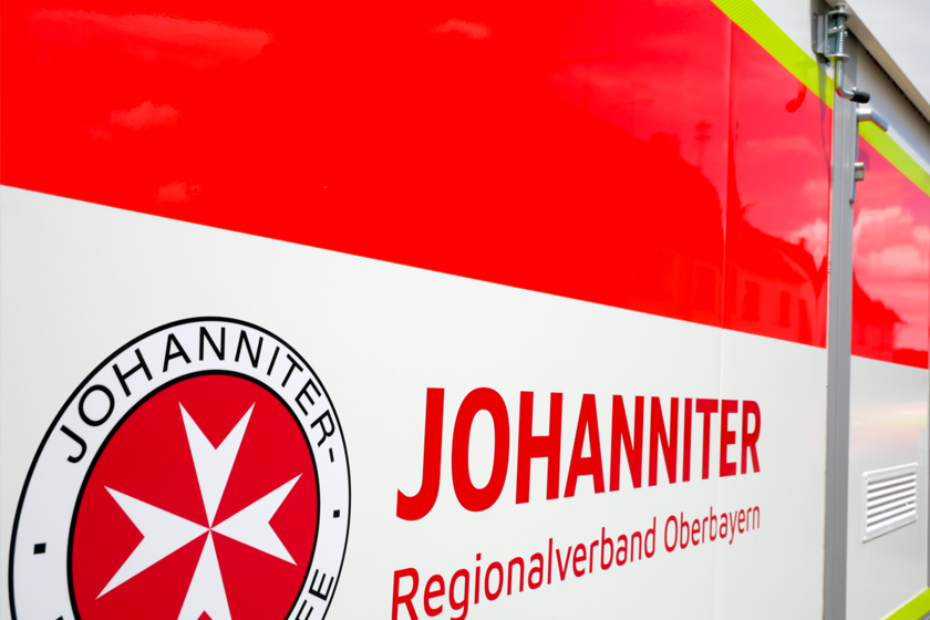 Johanniter-Logo und Schriftzug auf der roten Seitenfläche eines Einsatzfahrzeugs.