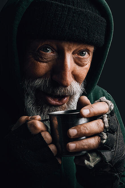 Ein Obdachloser mit einem Becher, an dem er sich wärmt