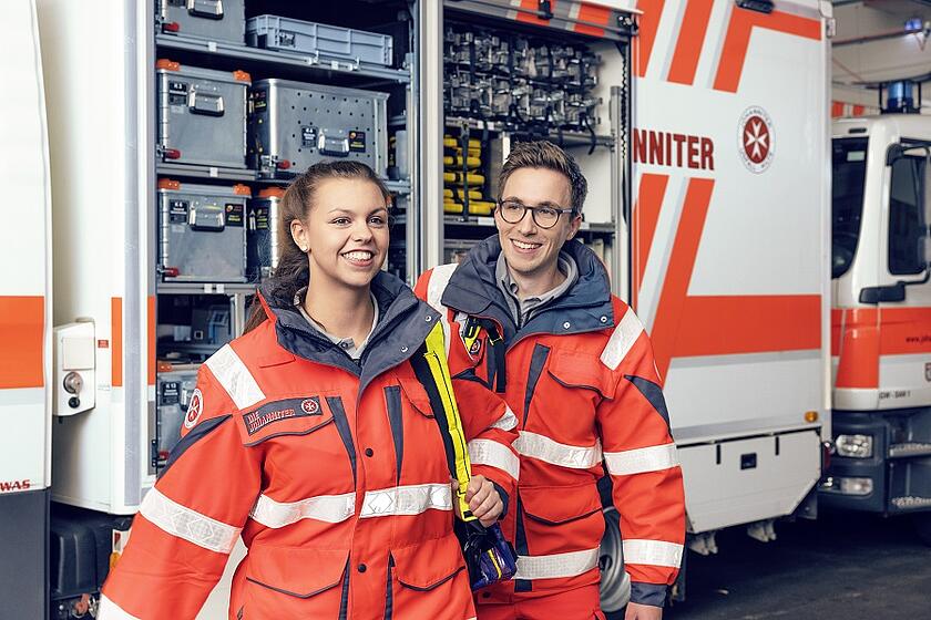 Zwei Ehrenamtliche der Johanniter vor einem Einsatzwagen