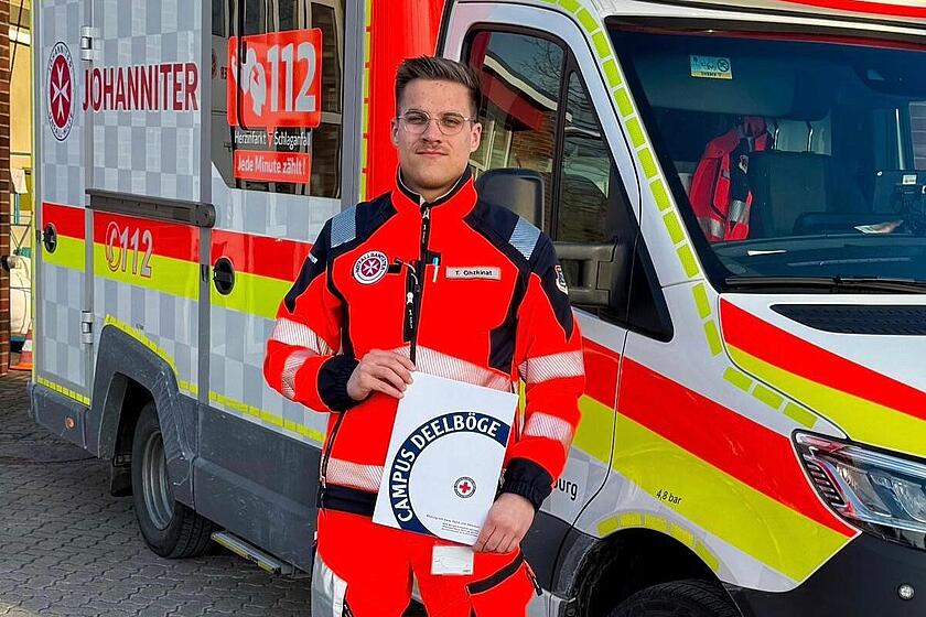 Ein Auszubildender zum Notfallsanitäter hält sein Abschlusszeugnis in der Hand