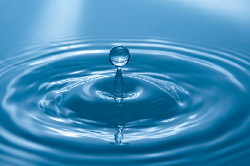 Ein Tropfen fällt auf eine Wasseroberfläche. Das ganze Bild ist blaugefärbt.