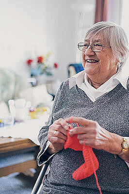 Eine Seniorin in grauem Pullover strickt