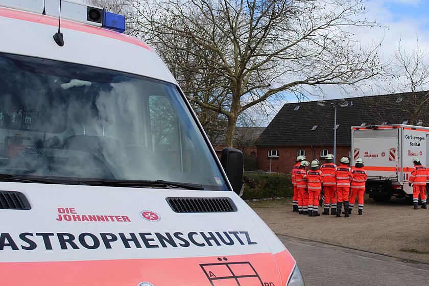 Katschutzfahrzug im Vordergrund, hinten Helfende um Sanfahrzeug Transport herum