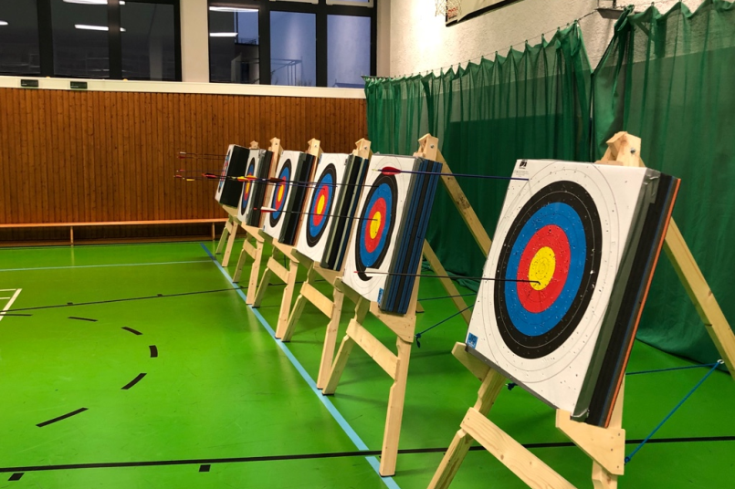 6 Bogenschießstände in einer Sporthalle mit grünem Boden.