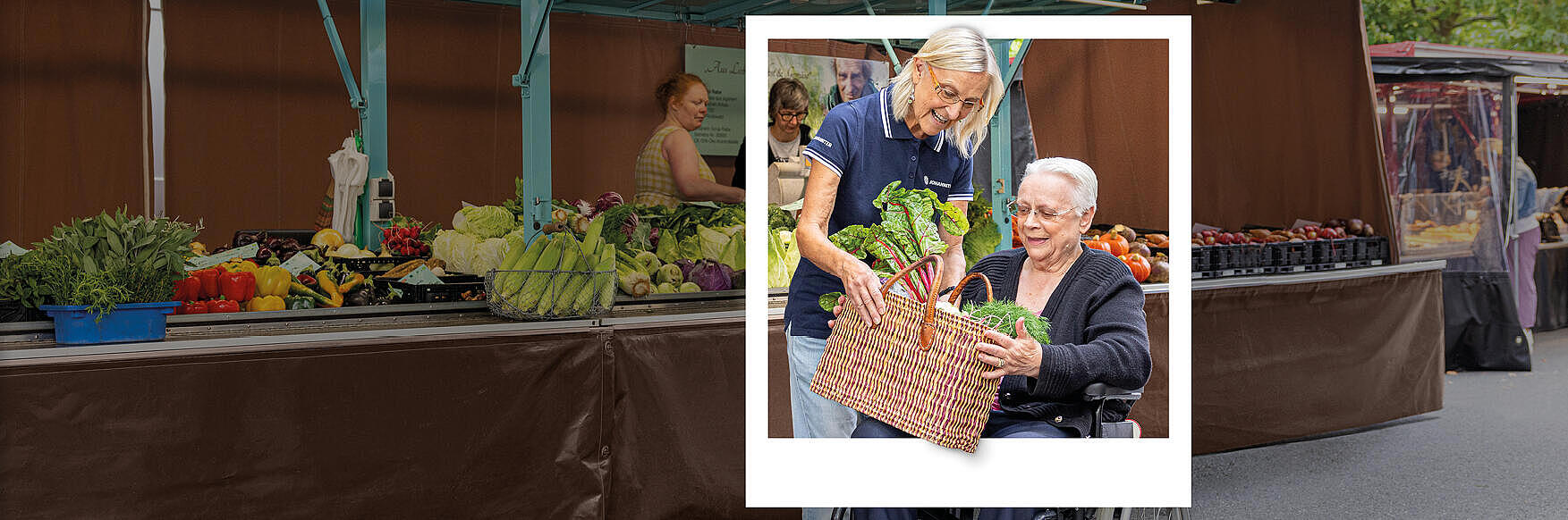 Eine ehrenamtlich Tätige im sozialen Dienst bei den Johannitern besucht einen Marktstand gemeinsam mit einer Frau im Rollstuhl.