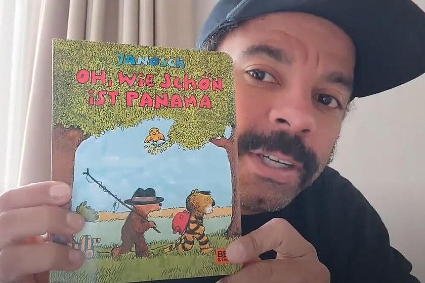 Ein Mann hält lächelnd ein bunt illustriertes Kinderbuch mit dem Titel „Oh, wie schön ist Panama“ in die Kamera.