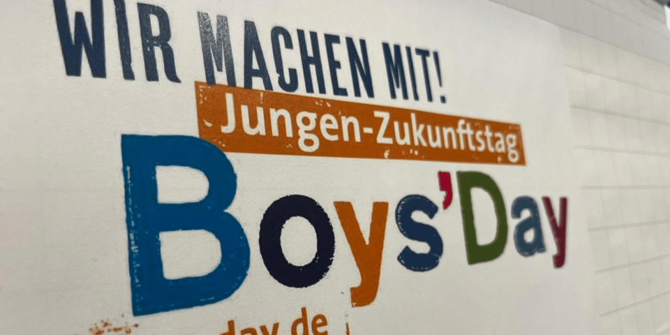 Plakat mit Schriftzug "Boys'Day" an einer weißen Wand.