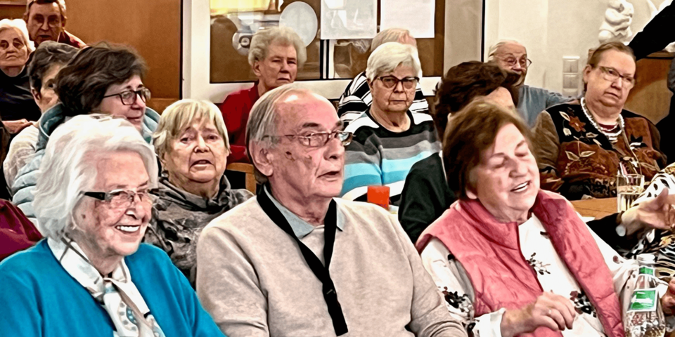 Lachende und schunkelnde Menschen sitzend an Tischen