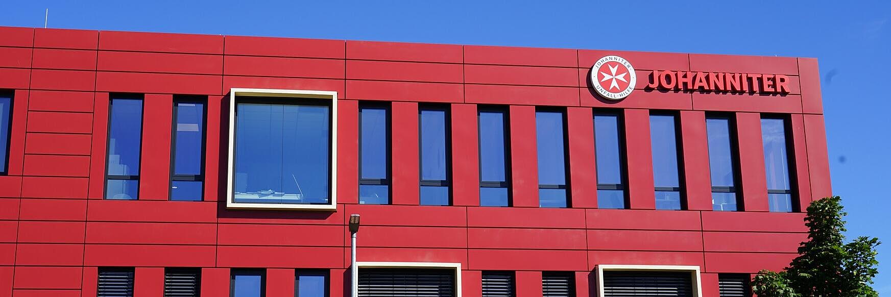 Man sieht ein großes, rotes Gebäude mit dem Schriftzug "Johanniter"