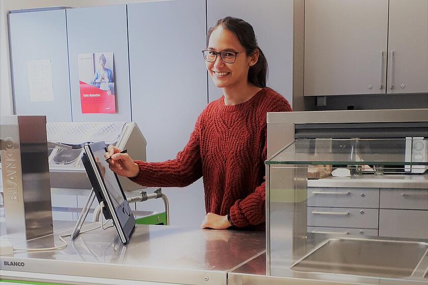 Eine Frau steht hinter einer Essenstheke und bedient einen Bildschirm.