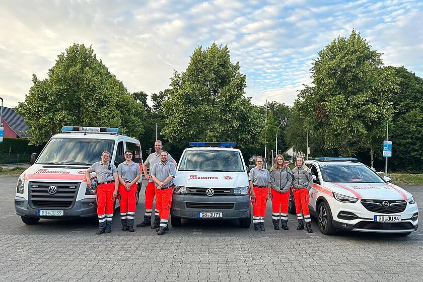 Sieben Menschen in Einsatzkleidung stehen vor drei Fahrzeugen mit Johanniter-Logos