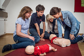 Jugendliche üben unter Anleitung die Herz‑Lungen‑Wiederbelebung an Kinder-Übungspuppen.