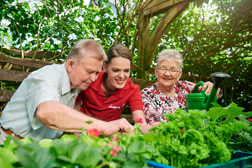 Eine Pflegerin der Johanniter ist mit zwei älteren Pflegepersonen im Garten.