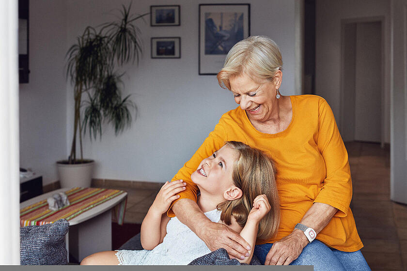 Eine Großmutter mit ihrer Enkelin. Die Oma trägt einen Hausnotruf-Sender am Handgelenk.
