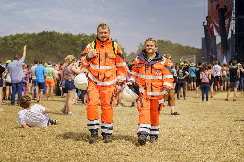 Zwei ehrenamtliche Mitarbeitende im Sanitätsdienst spazieren über ein Festivalgelände.