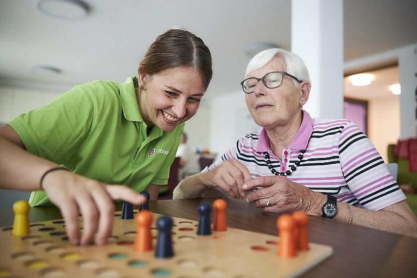 Eine Pflegekraft spielt mit einer älteren Frau ein Brettspiel