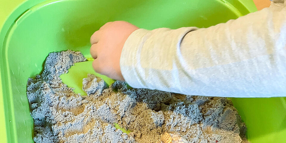 Kinderhände dekorieren eine grüne Schale mit Sand mit Muscheln