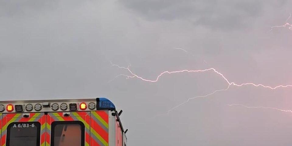 Ein Rettungswagen bei Gewitter auf der Straße. über ihm ein heller Blitz am Himmel.