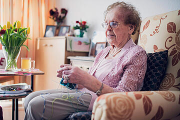Dame mit Strickzeug im Sessel im Bewohnerzimmer