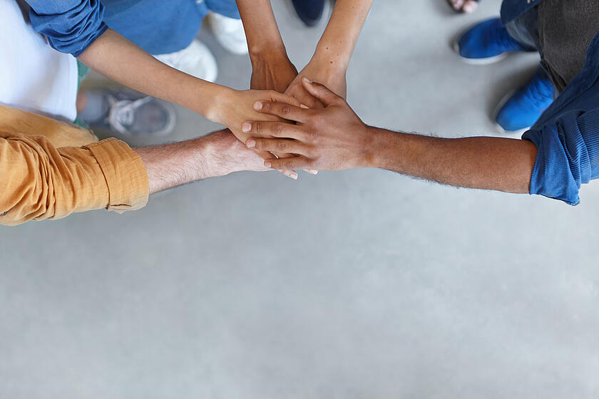 5 Leute stehen im Kreis und legen ihre Hände aufeinander.