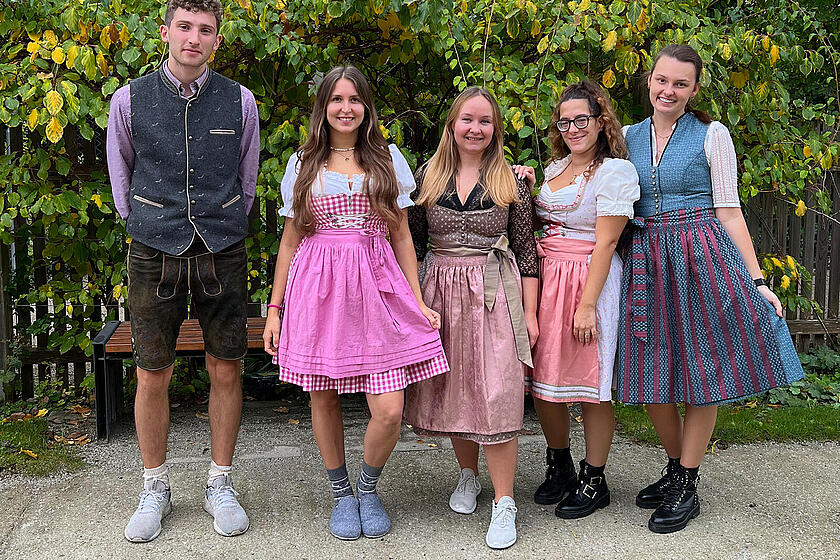 4 Leute stehen in Tracht auf einem Feldweg mit einer grünen Hecke im Hintergrund.