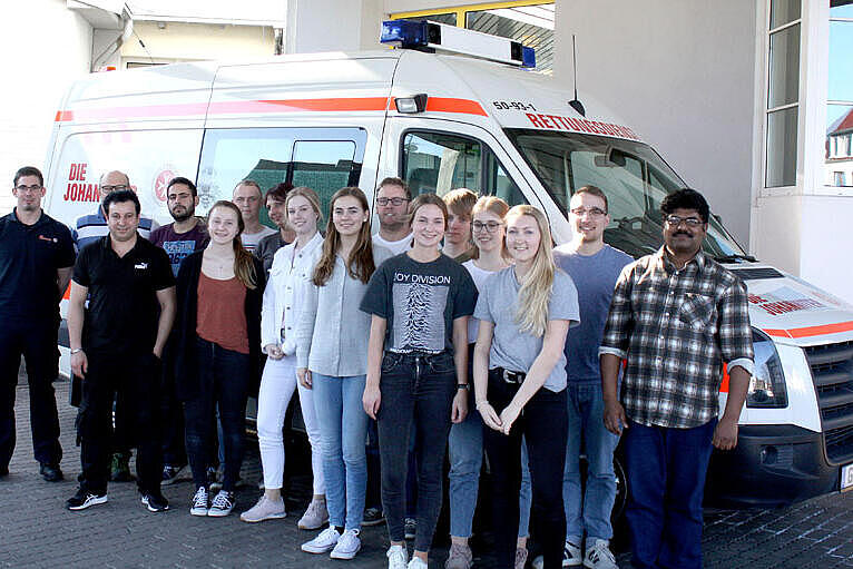 Gruppenbild der erfolgreichen Absolventenklasse vor einem Einsatzfahrzeug der Johanniter. 