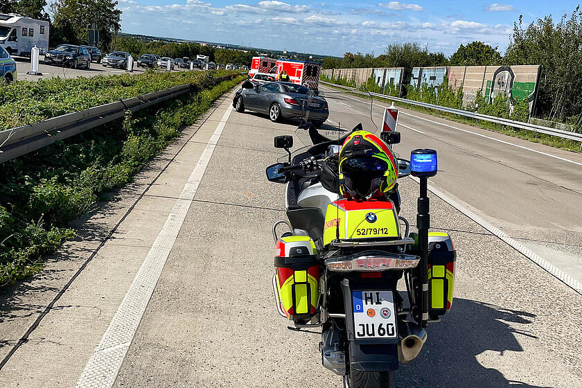 Ein Johanniter-Motorrad auf der Autobahn. Dahinter ein verunfallter Wagen und ein Rettungswagen.