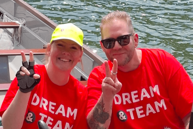 Zwei Personen in roten T‑Shirts zeigen Victory‑Zeichen und lächeln im Boot.