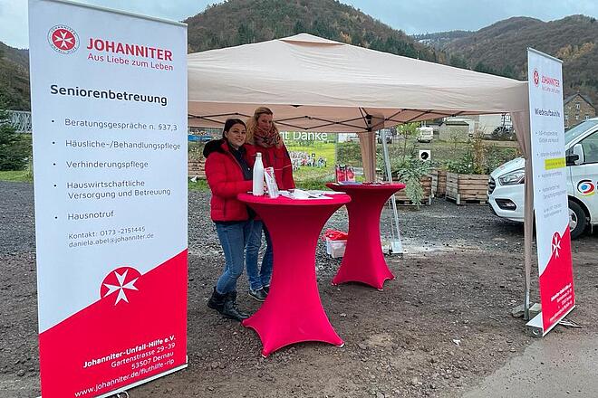 Zwei Mitarbeitende der Johanniter stehen am Stand der Infobustour der Johanniter-Fluthilfe