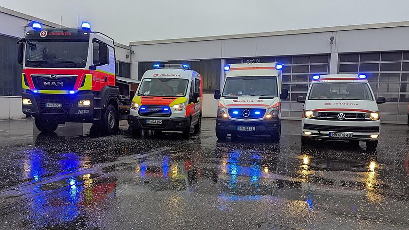 vier Einsatzwagen der Johanniter stehen auf einem Hof mit eingeschalteten Blaulicht. Darunter ein Rettungswagen, ein Krankentransportwagen, ein Wechsellader und ein Führungsfahrzeug.