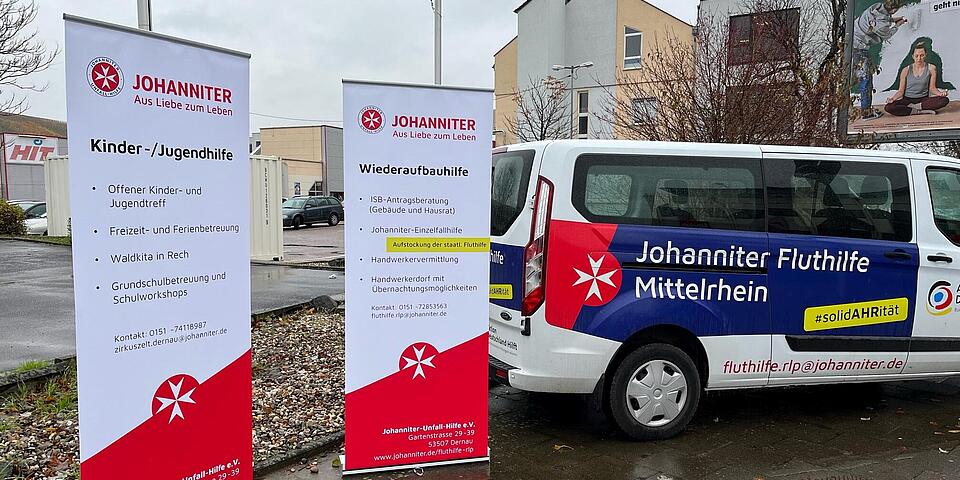 Ein Fahrzeug und zwei informative Roll-ups der Johanniter-Fluthilfe auf einem Parkplatz