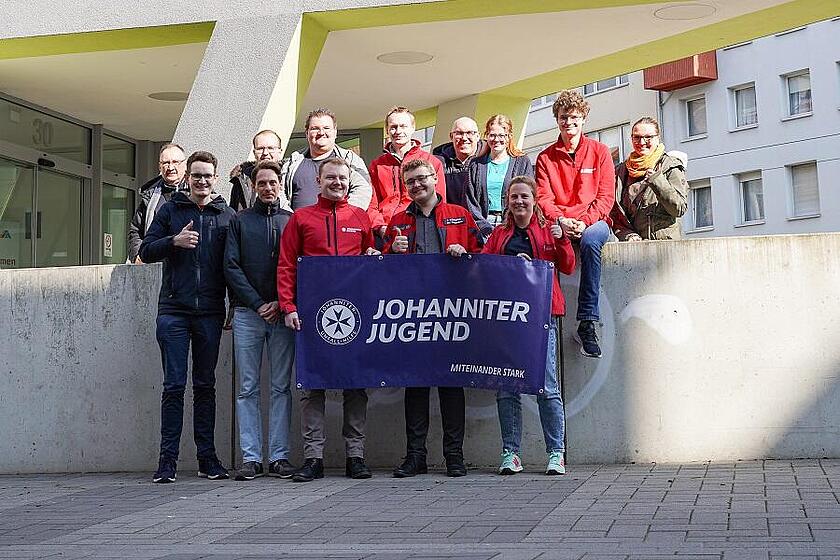 Mehrere Mitglieder der Johanniter-Jugend stehen in einer Gruppe in Braunschweig und halten eine Fahne in den Händen