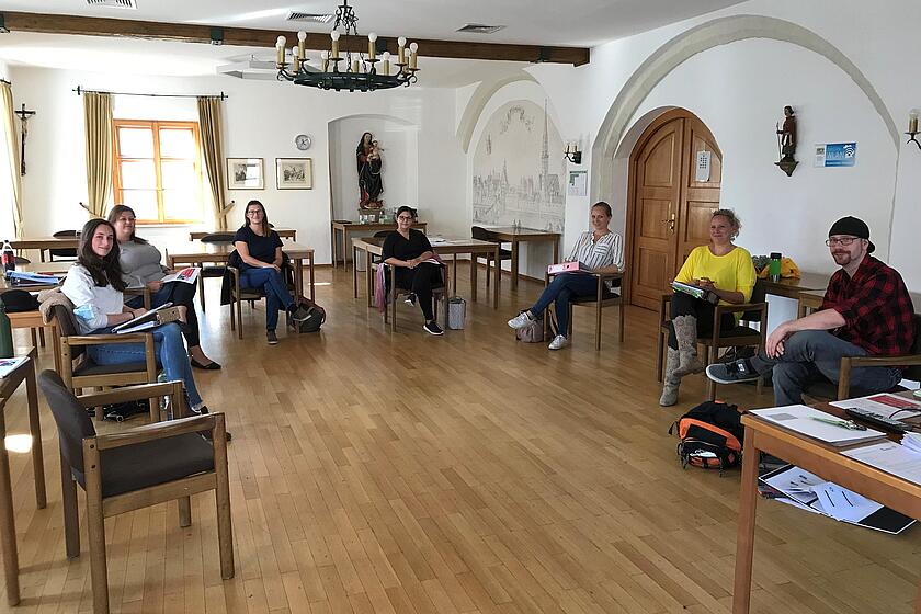 Mehrere Leute sitzen in einem Stuhlkreis in einem großen Raum.