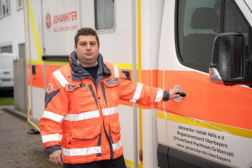 Ein Johanniter in Einsatzkleidung ist dabei die Tür zu einem Einsatzfahrzeug zu öffnen.