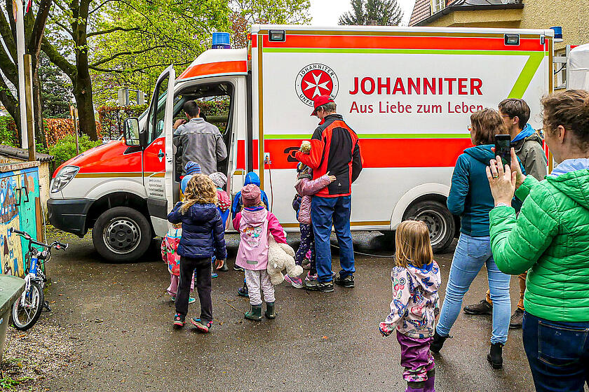 Mehrere kleine Kinder schauen gespannt auf einen Johanniter Rettungswagen.