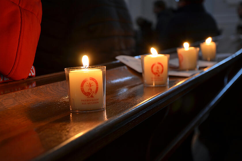 4 Friedenslichter stehen in der Kirche auf der Bank nebeneinander