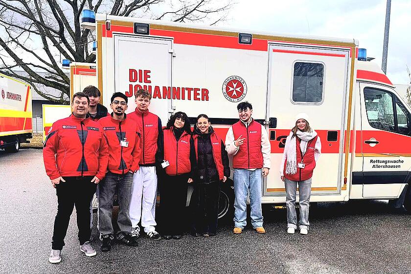 Mehrere junge Leute in Johanniter Kleidung stehen vor einem Johanniter Einsatzfahrzeug.