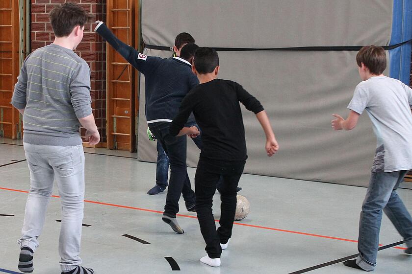 Eine Gruppe an Jungen spielen in einer Sporthalle Fußball.