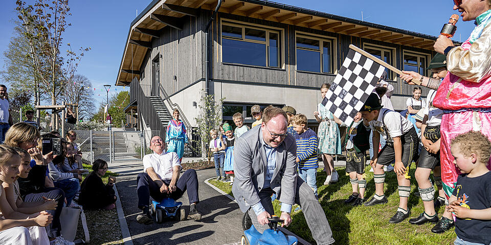 Kinder jubeln den Bürgermeistern zu, die auf Bobbycars um die Wette fahren.