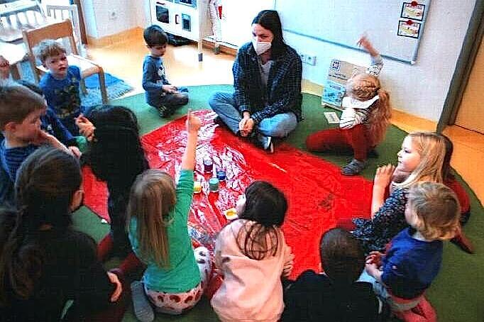 Eine Kindergartengruppe sitzt im Kreis um bunte Malfarben.
