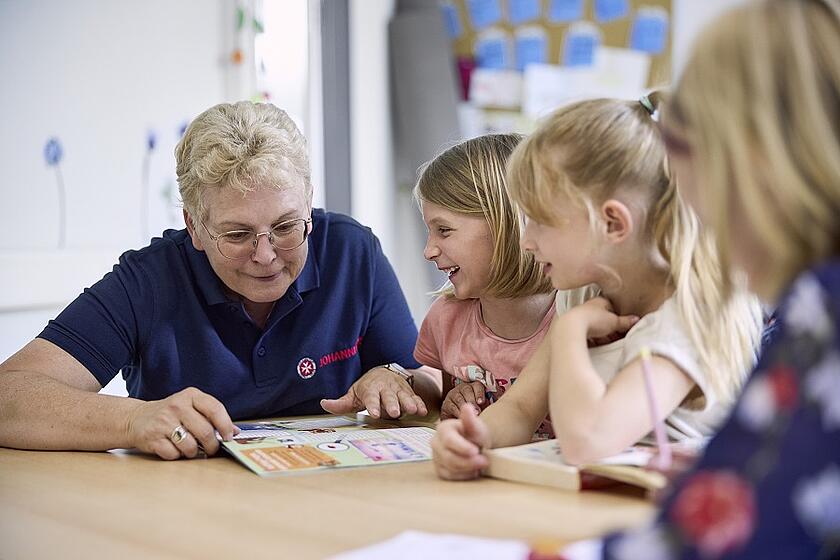Eine Mitarbeiterin in der Johanniter Ganztagsbetreuung und Kinder besprechen ein Magazin.