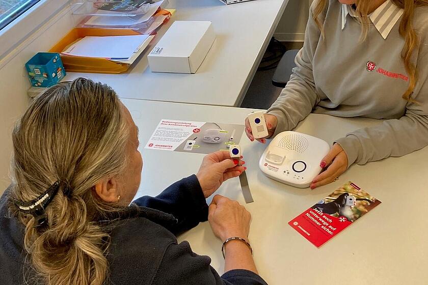 Eine Mitarbeiterin der Johanniter im Ahrtal erklärt einer Dame den Hausnotruf