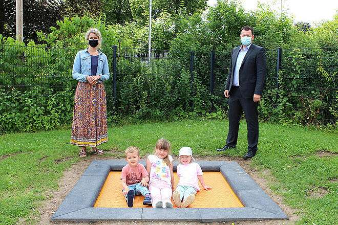 Drei Kinder sitzen auf dem neuen Trampolin, an der Seite steht die Kita-Leitung und der Klinikgeschäftsführer des Hildesheimer Helios Klinikums.